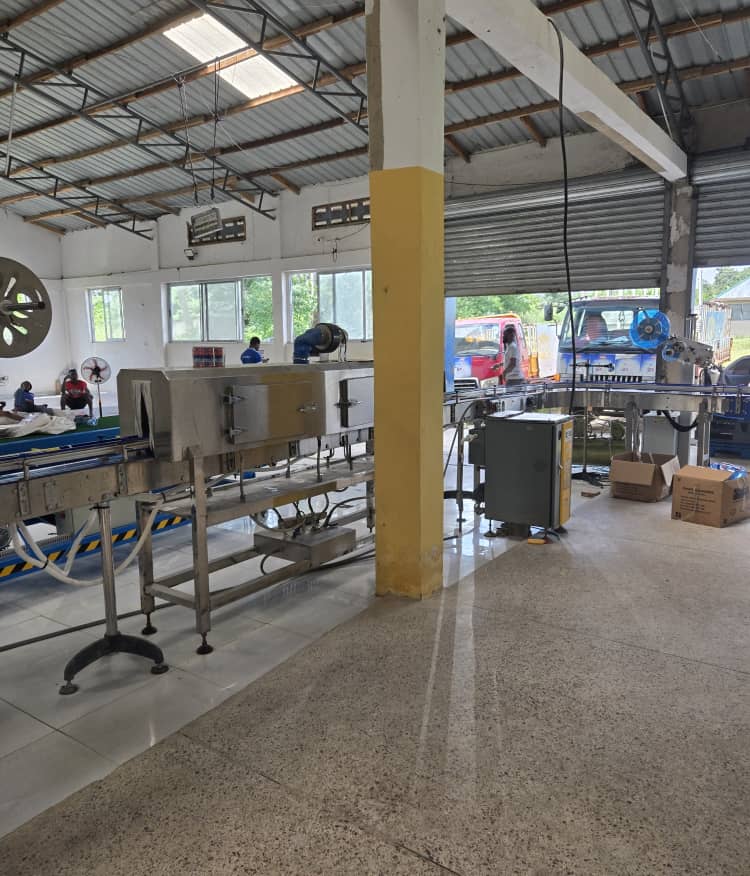 Stainless steel conveyor machinery in a factory with trucks visible through an open door.